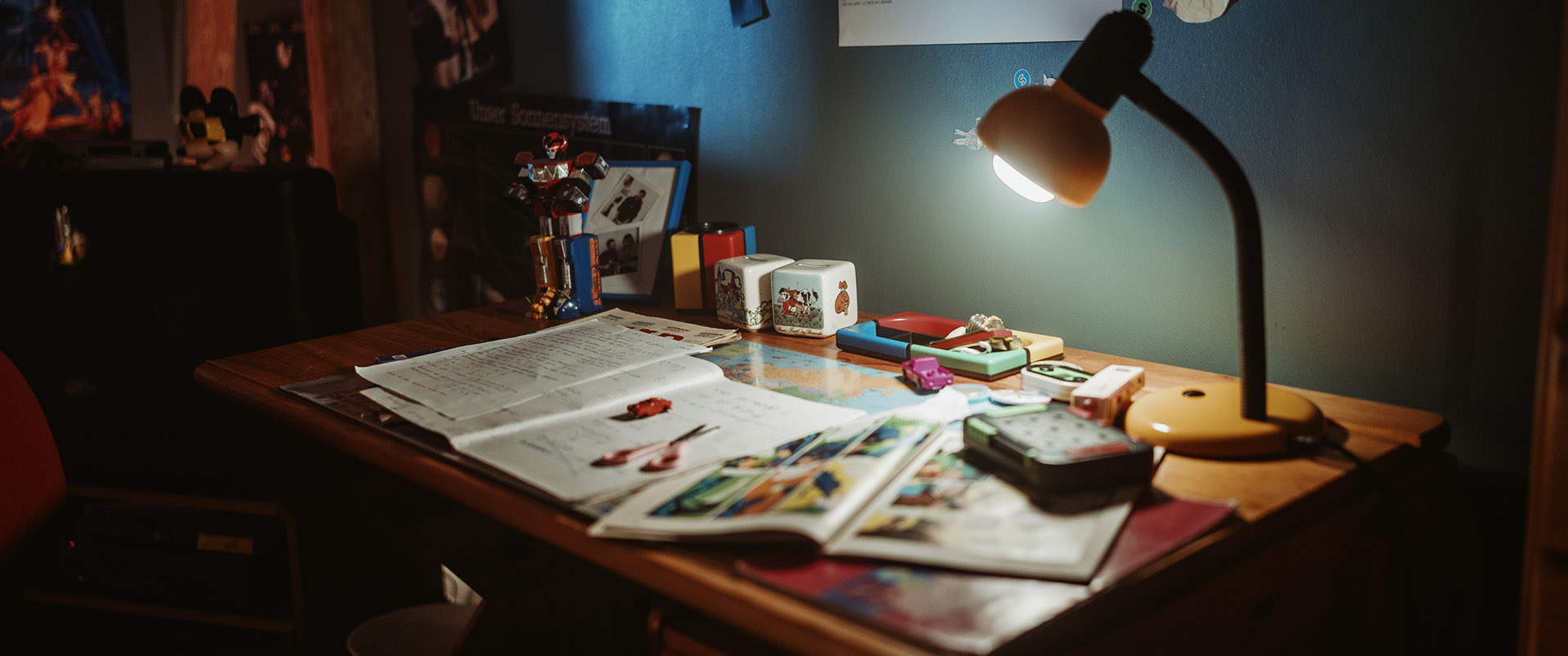 A desk lamp lighting a cluttered childhood desk of toys and comics